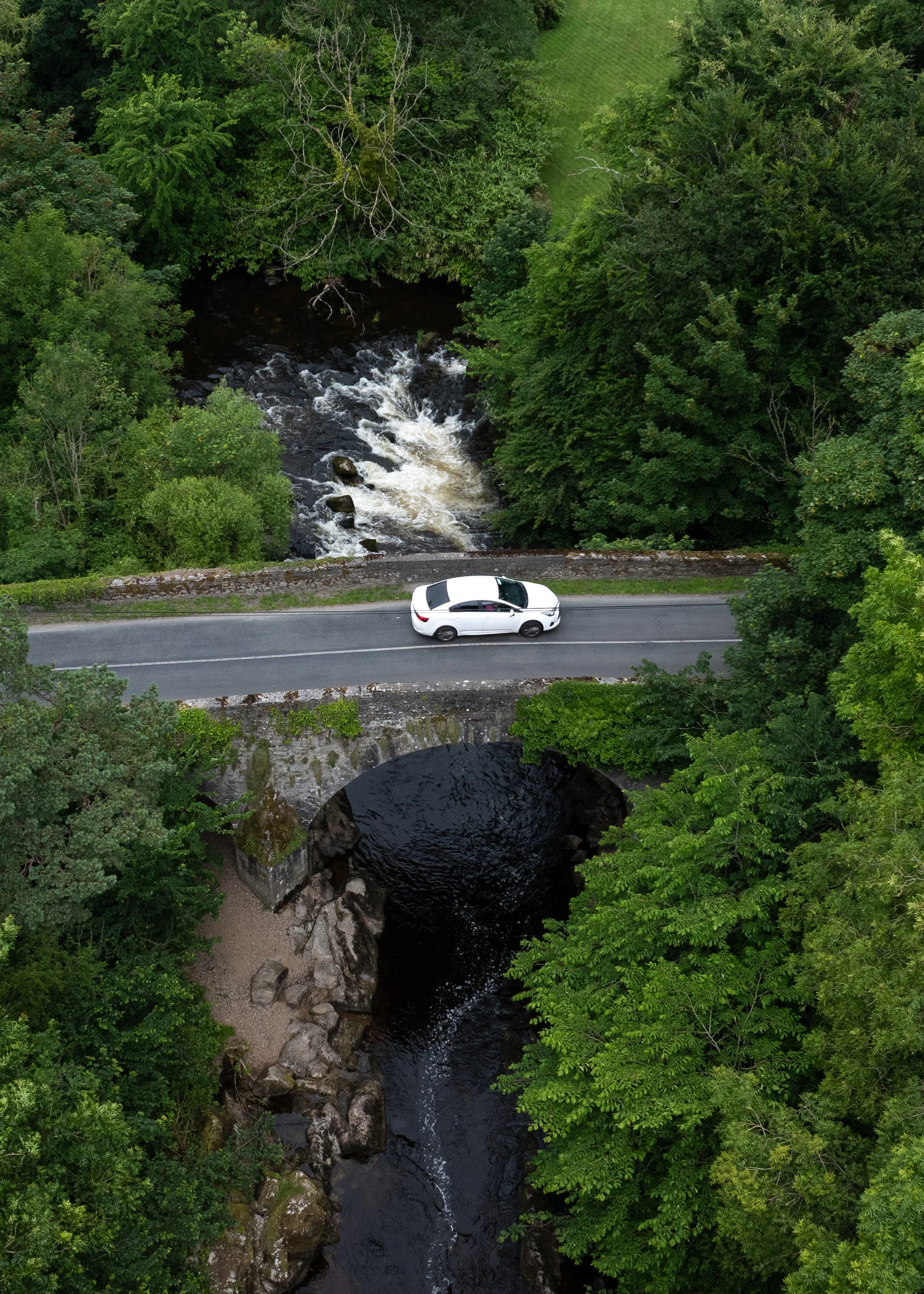 Car crossing stone bridge over river gorge surrounded by trees